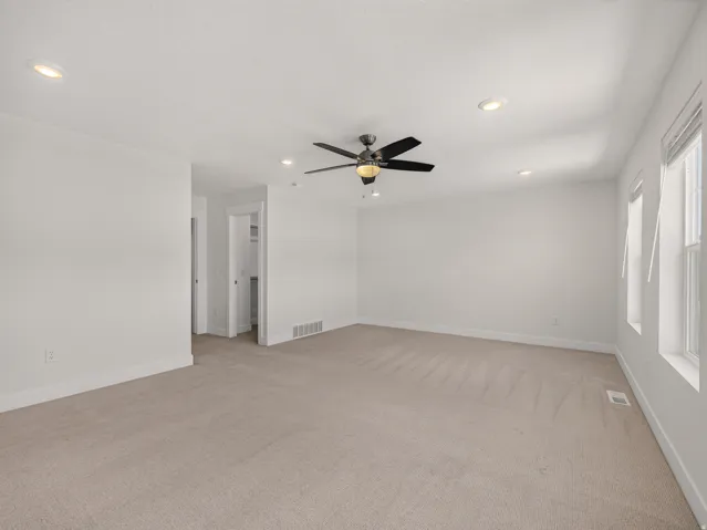 Spacious room featuring neutral carpeting, white walls, recessed lighting, and a ceiling fan