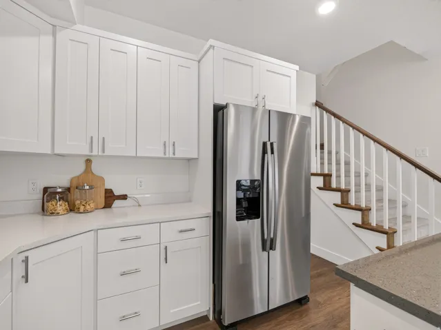 Modern kitchen featuring white shaker cabinetry, stainless steel refrigerator, white countertops, and wood-finish flooring