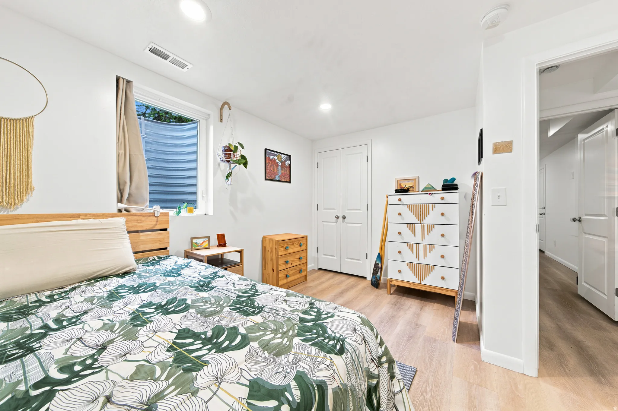 Bright bedroom featuring light wood-finish flooring, white walls, a window with a window well, and bi-fold closet doors