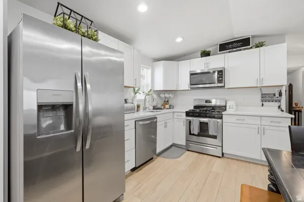 Modern kitchen featuring white cabinetry, light countertops, stainless steel appliances, and light wood-finish flooring