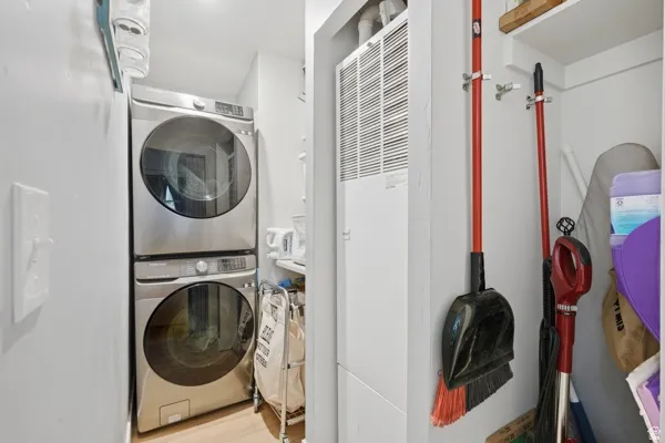 Dedicated laundry area featuring a stacked washer and dryer combination, light wood-finish flooring, and white walls