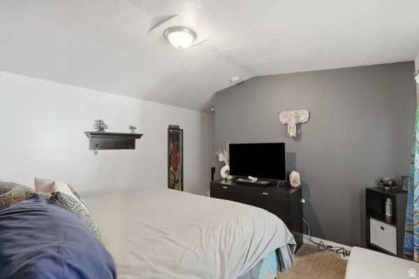 Bedroom featuring vaulted ceiling, neutral wall tones, and carpet flooring