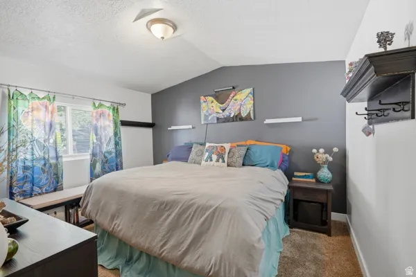 Carpeted bedroom featuring a window with a built-in bench, a dark accent wall, and a sloped ceiling