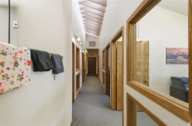 Vaulted ceiling with exposed wood beams, neutral wall paint, wood-framed doorways, and recessed lighting fixtures