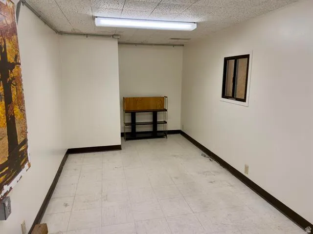 Room featuring white walls, dark trim, and a drop ceiling with recessed fluorescent lighting