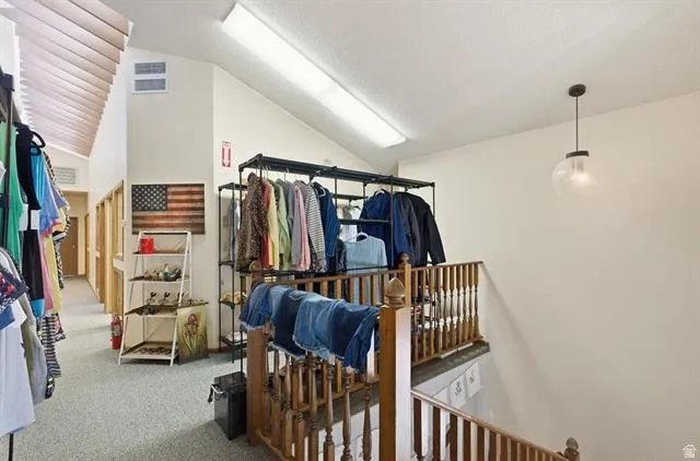 Carpeted upper level featuring a vaulted ceiling and an open hallway with wood railing