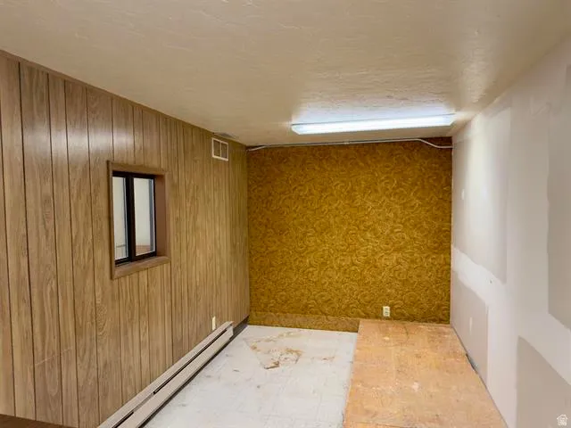 Interior room featuring wood-finish paneling, a small window with dark framing, and a wall-mounted baseboard heater