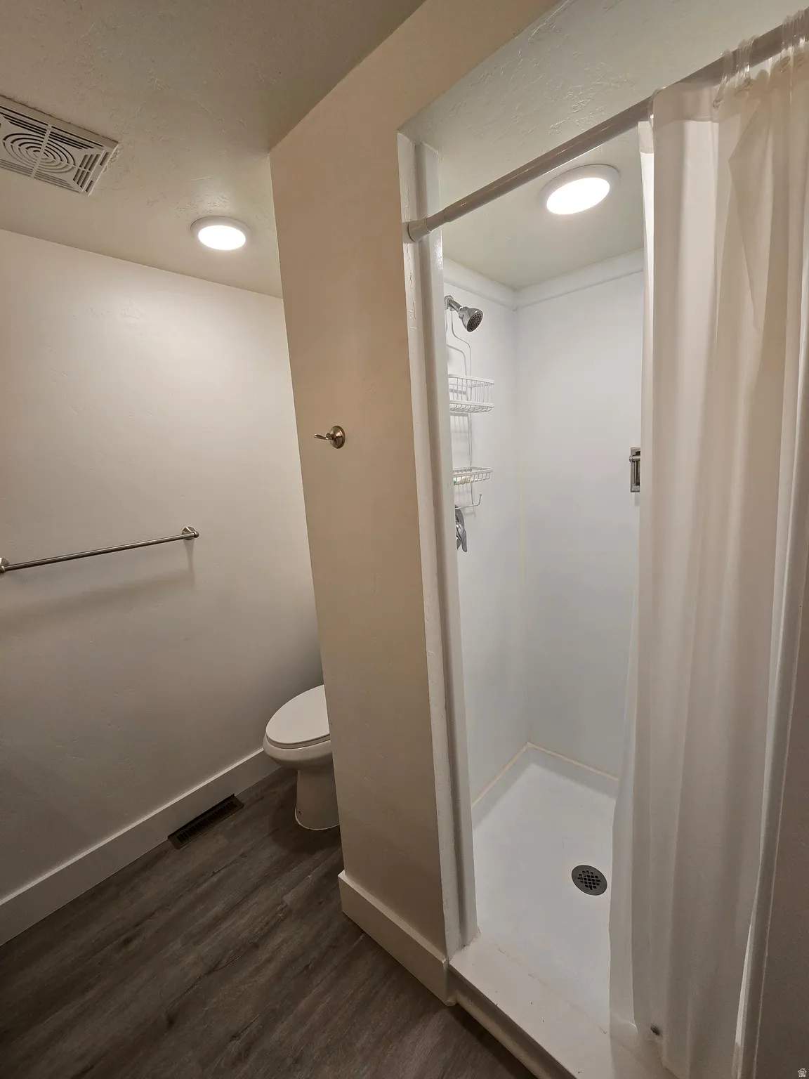 White-tiled shower with a curtain rod and overhead lighting
