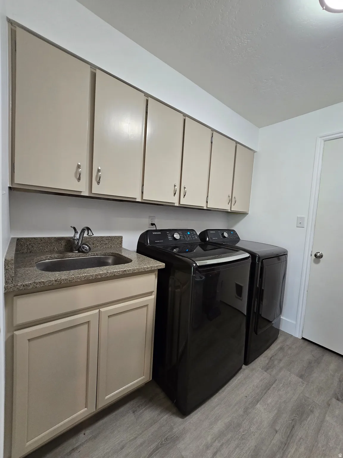 Utility area featuring ample cabinetry, a built-in sink with a stone-finish countertop, and wood-finish flooring
