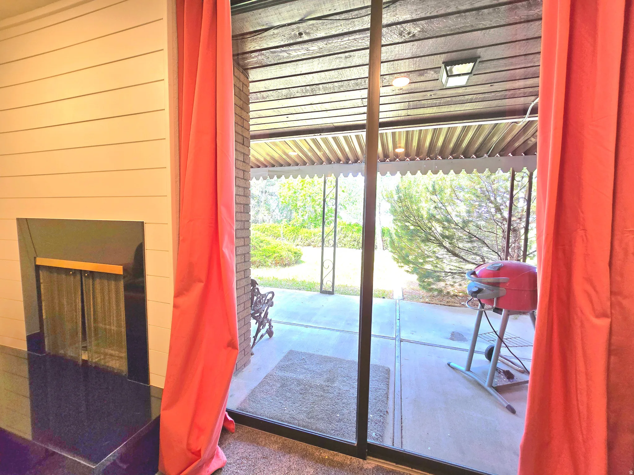 Sliding glass door opening to a covered patio featuring a wood-plank ceiling and brick-patterned wall