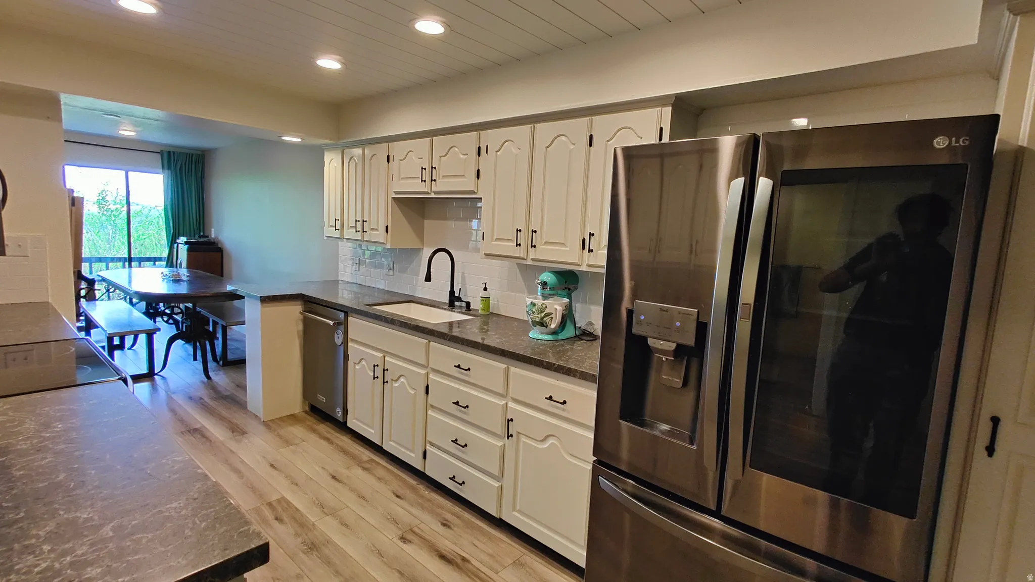 Kitchen featuring wood-finish flooring, white cabinetry, granite-style countertops, a stainless steel refrigerator, and a stainless steel dishwasher