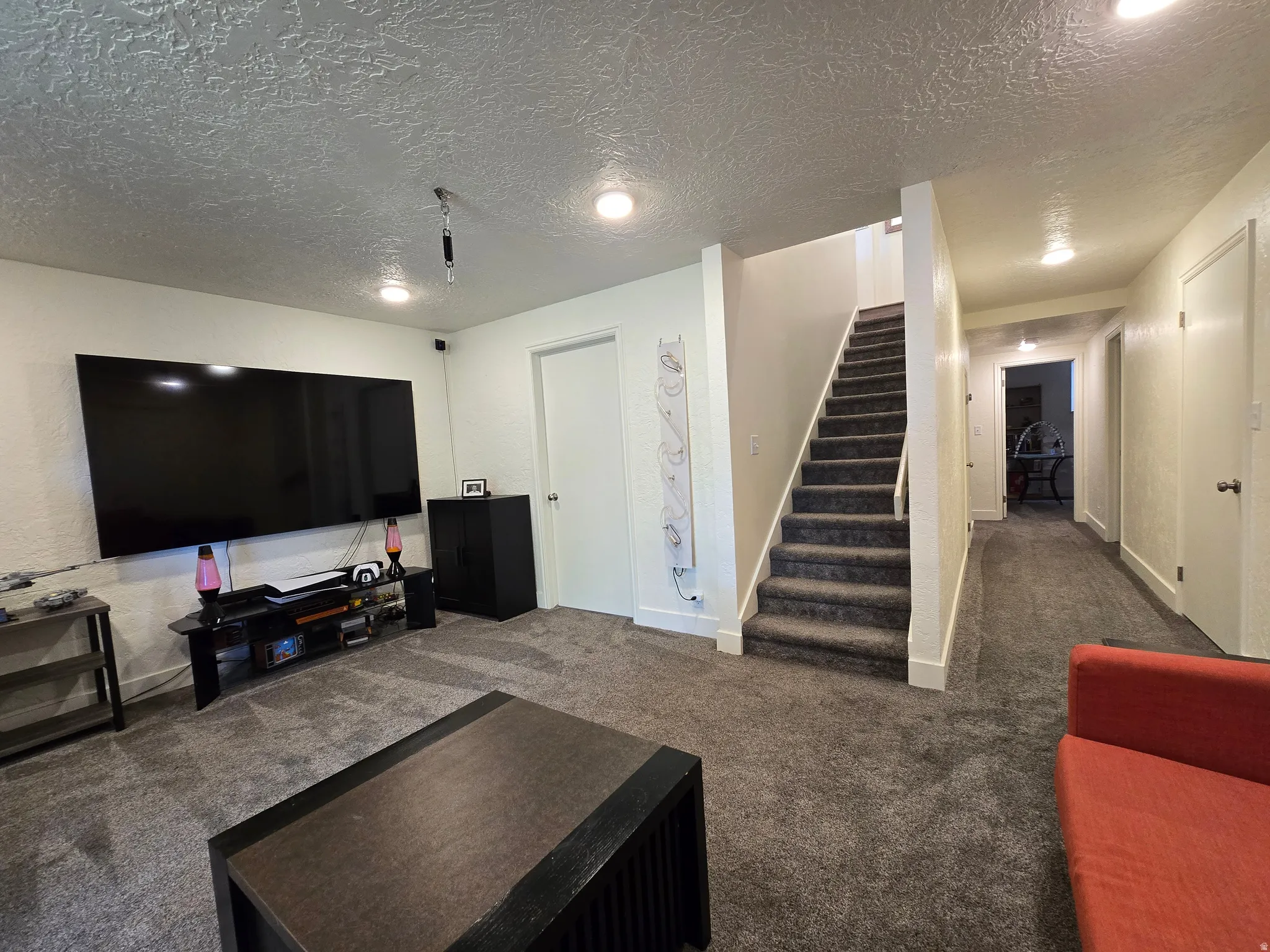 Carpeted living area featuring recessed lighting, a staircase with carpeting, and a hallway with additional lighting