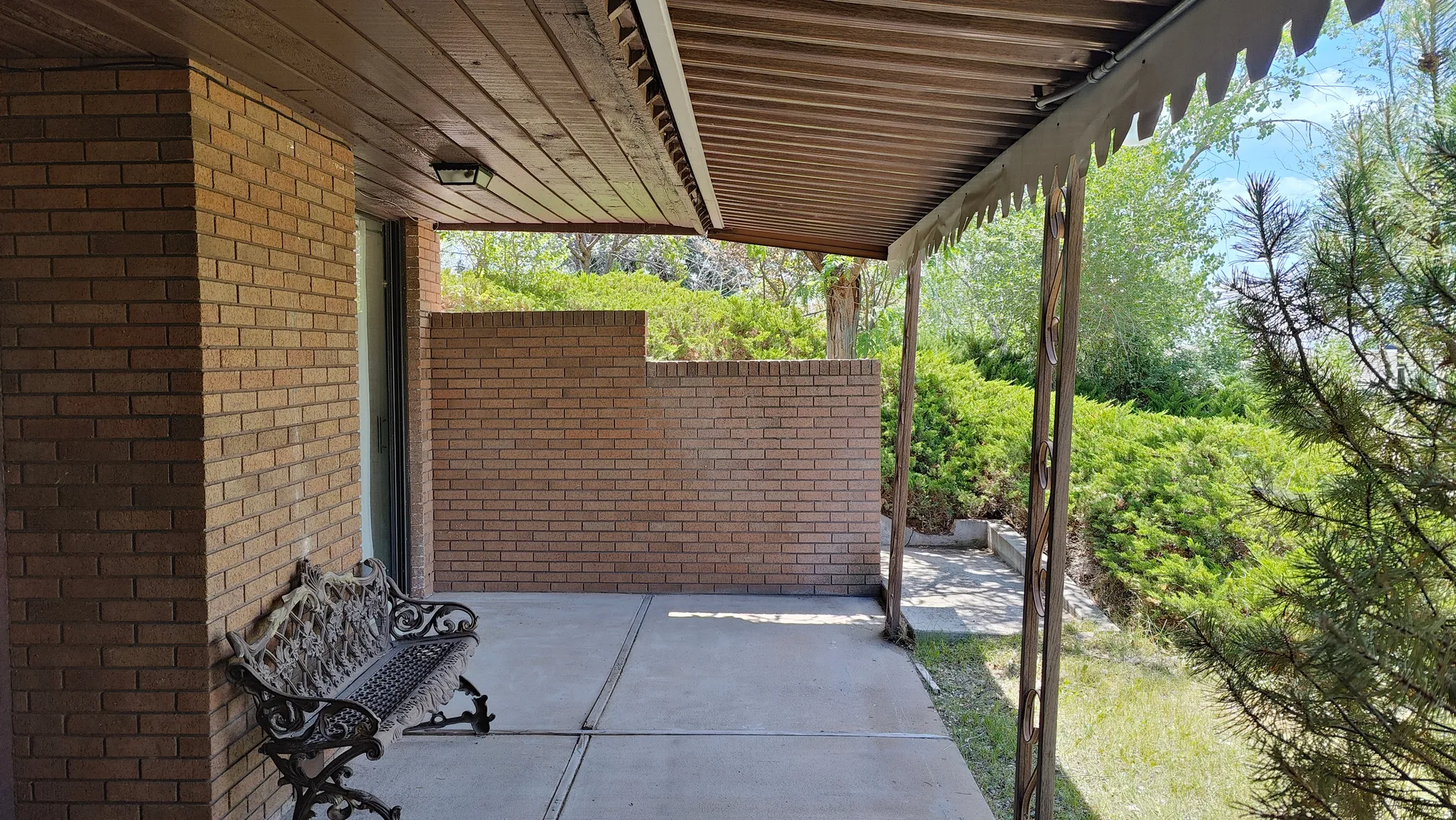Covered brick patio featuring a wood-finish ceiling with an attached light fixture, concrete flooring, and surrounding brick walls