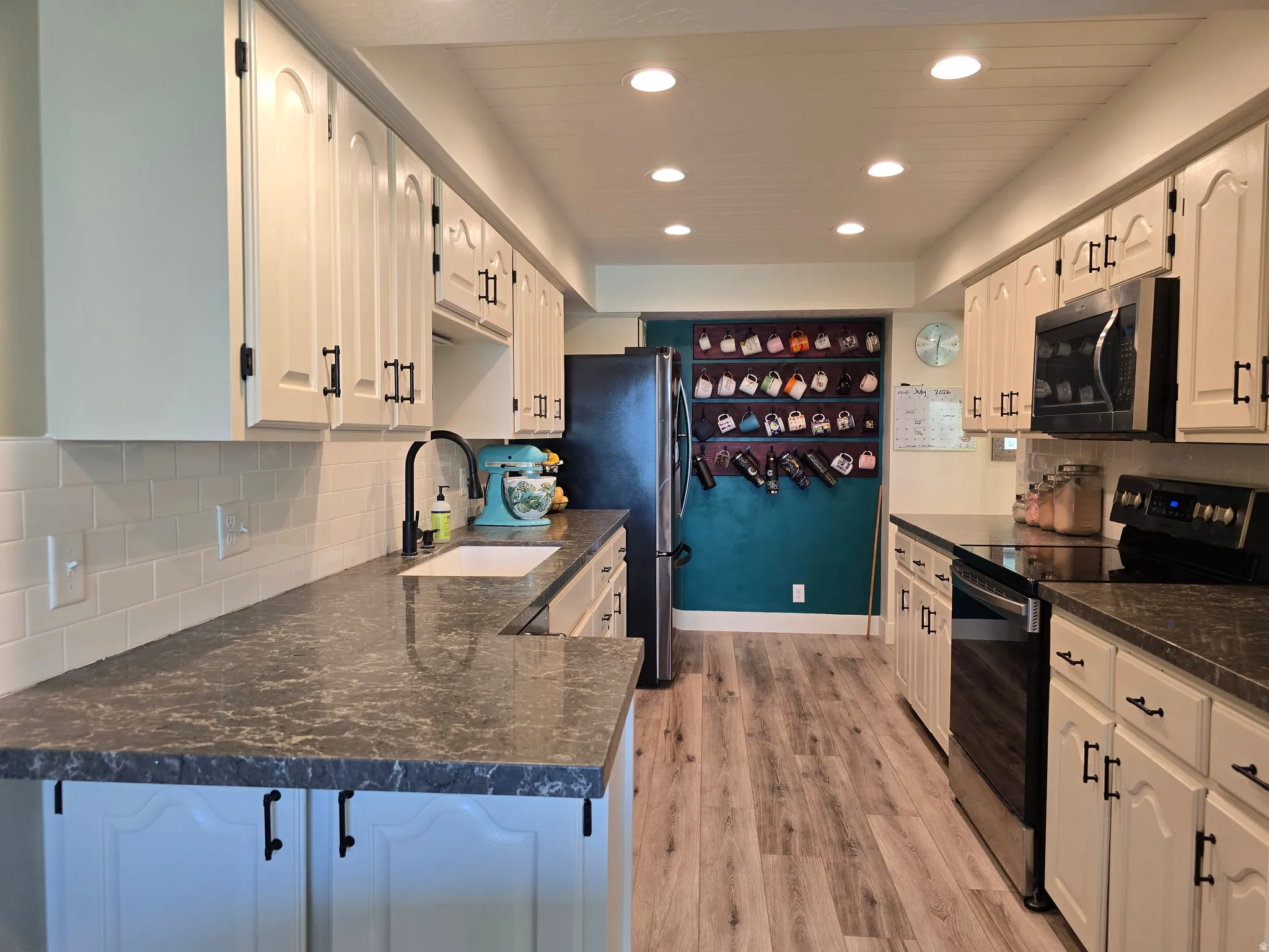 Modern kitchen featuring light-toned cabinetry with dark hardware, dark patterned countertops, and a white subway tile backsplash