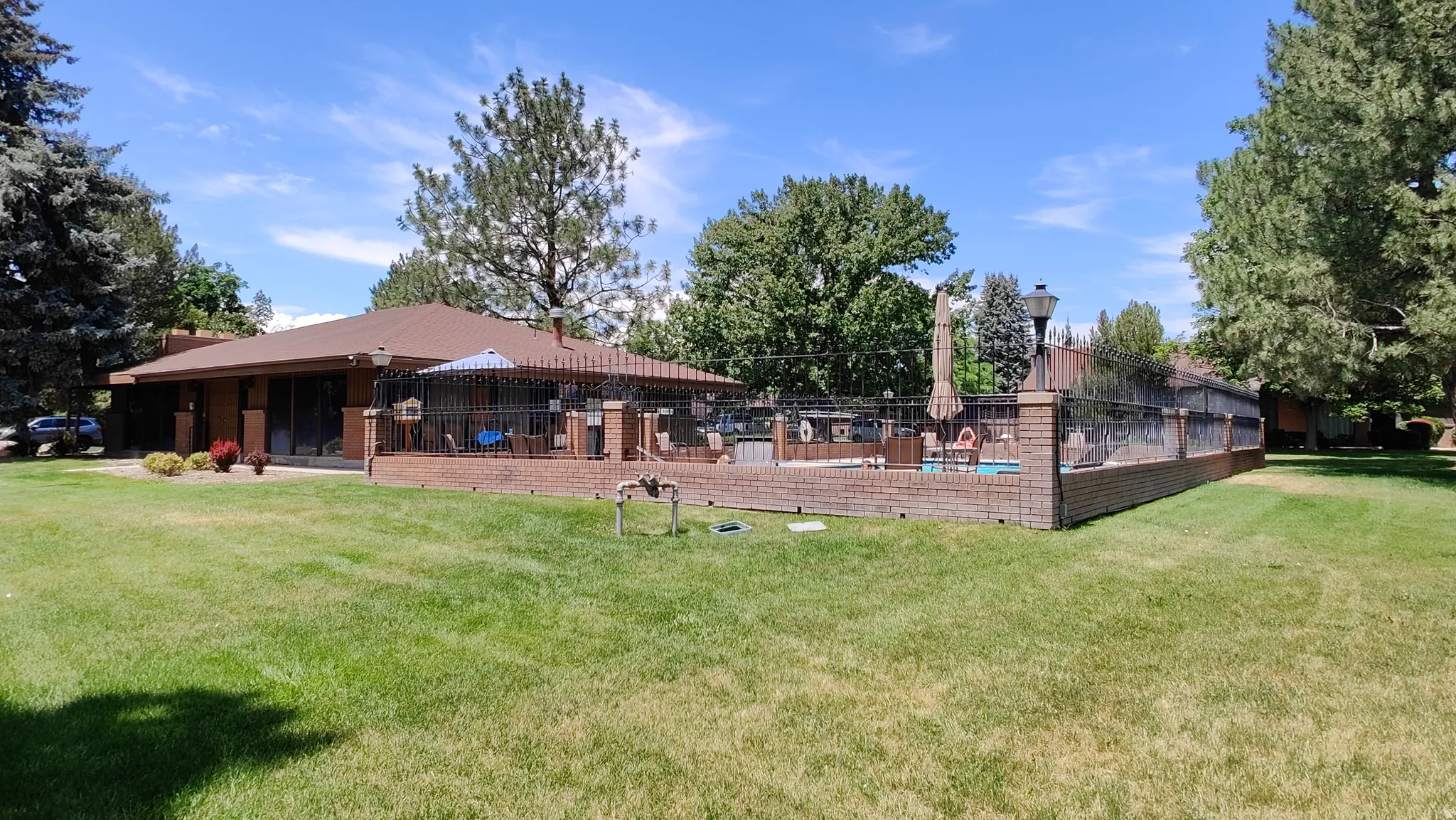 Expansive green lawn bordering a brick patio featuring a pool and perimeter fencing