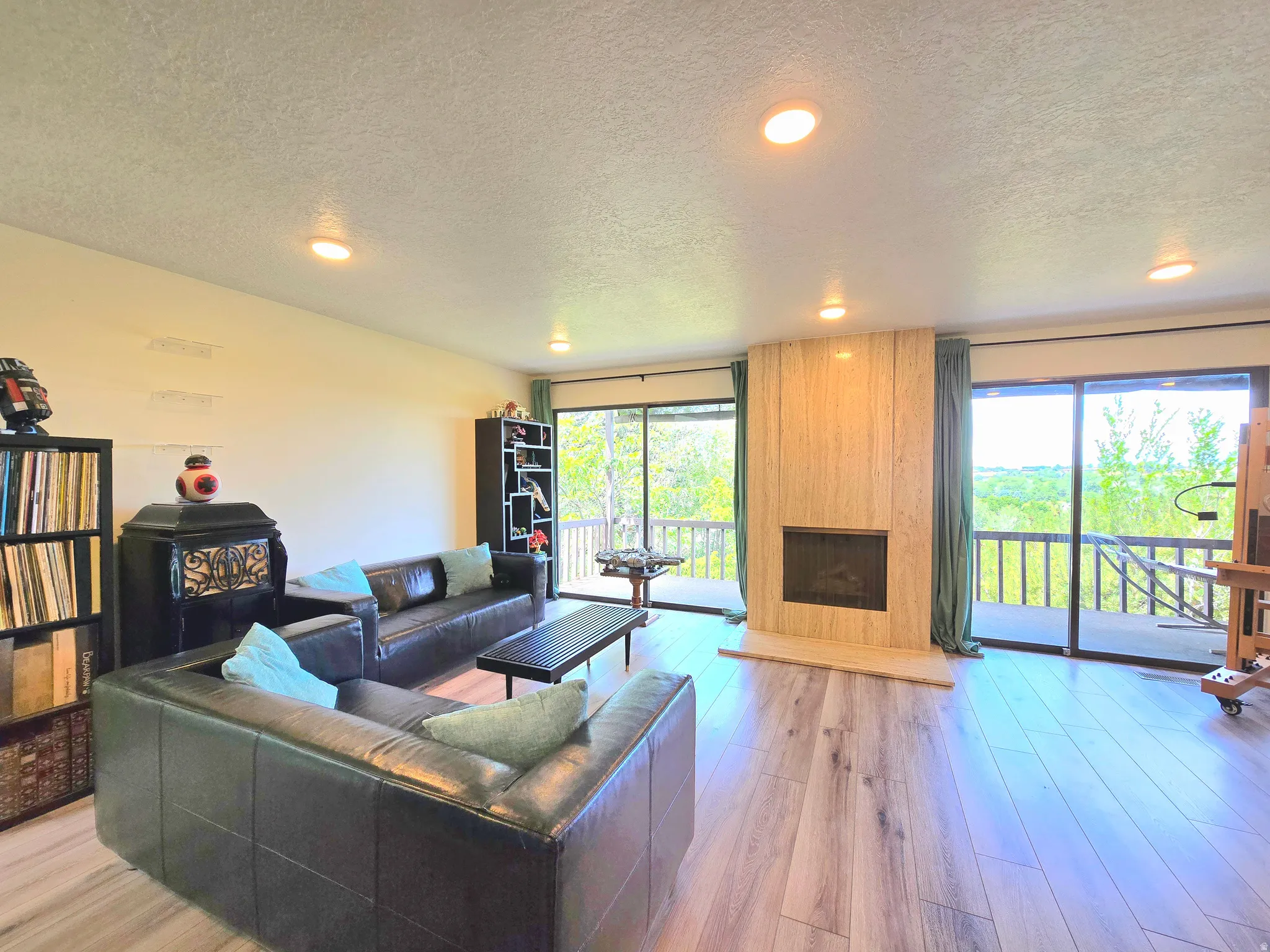 Living area featuring wood-finish flooring, a prominent fireplace with a light-colored surround, and recessed ceiling lighting