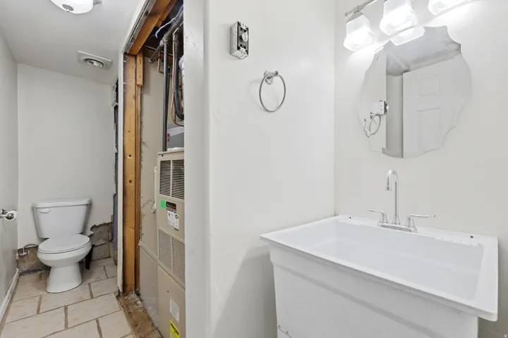 Utility sink with a chrome faucet, illuminated by a three-bulb vanity light fixture