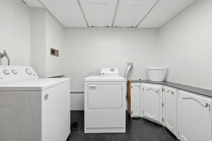 Dedicated laundry area featuring a washer and dryer, white paneling, built-in white cabinetry, a dark countertop, and dark flooring