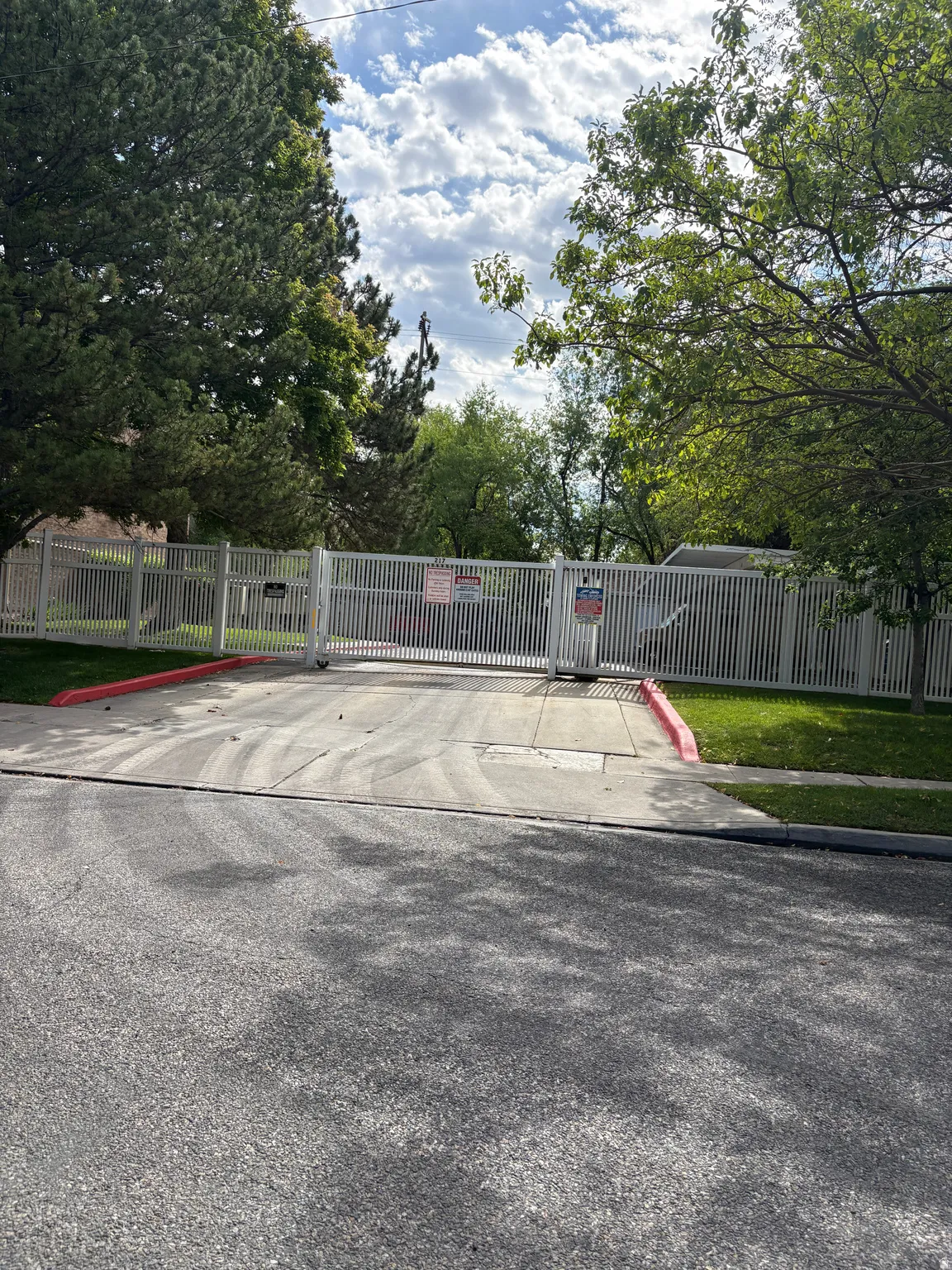 Gated entry with a white metal fence and mature trees