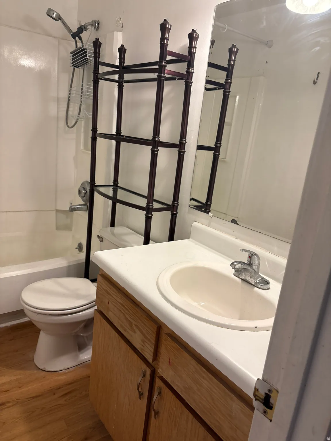 Bathroom featuring a white vanity with integrated sink, wood-finish flooring, and a shower-tub combination with a wall-mounted showerhead