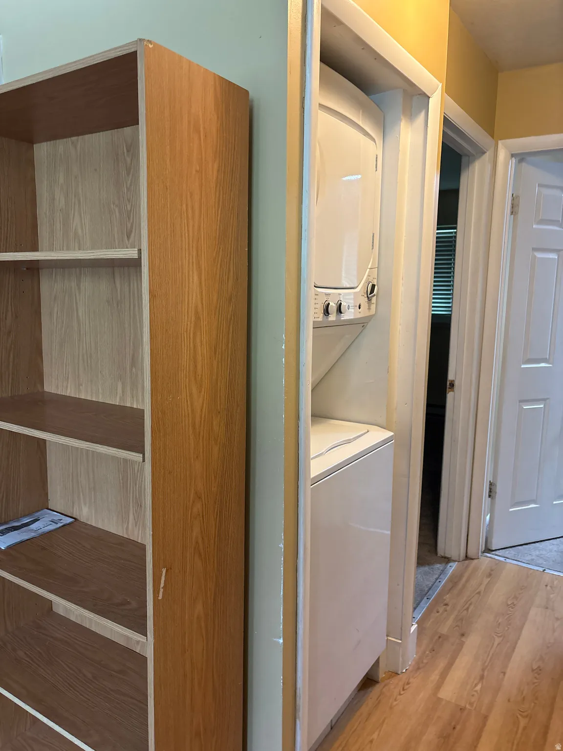 Dedicated laundry closet featuring a white stacked washer and dryer unit, wood-finish flooring, and light-toned walls
