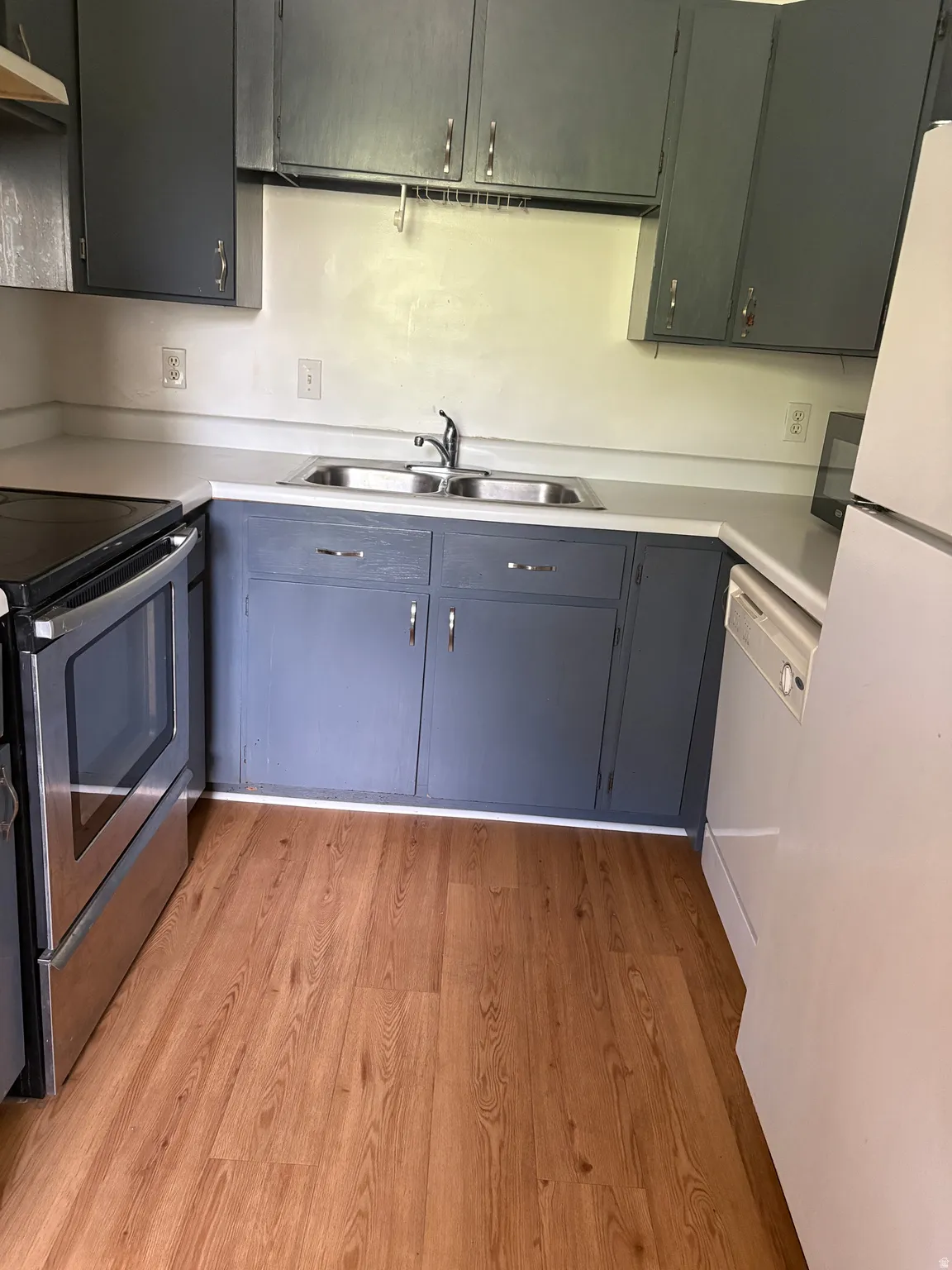 Kitchen featuring wood-finish flooring, dual basin stainless steel sink, and perimeter cabinetry with light countertops
