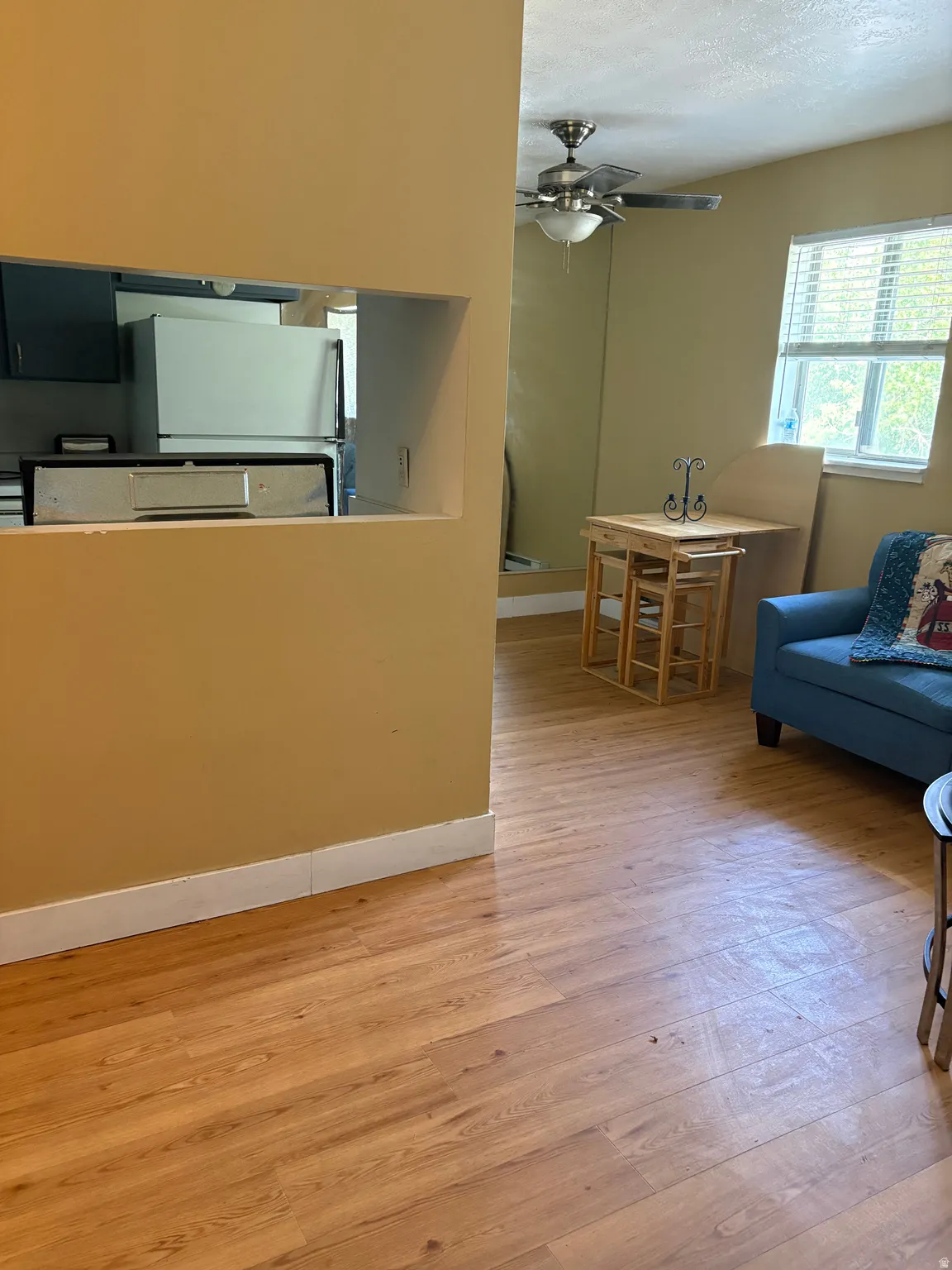 Interior space featuring wood-finish flooring, a pass-through window to the kitchen, and a ceiling fan with integrated lighting