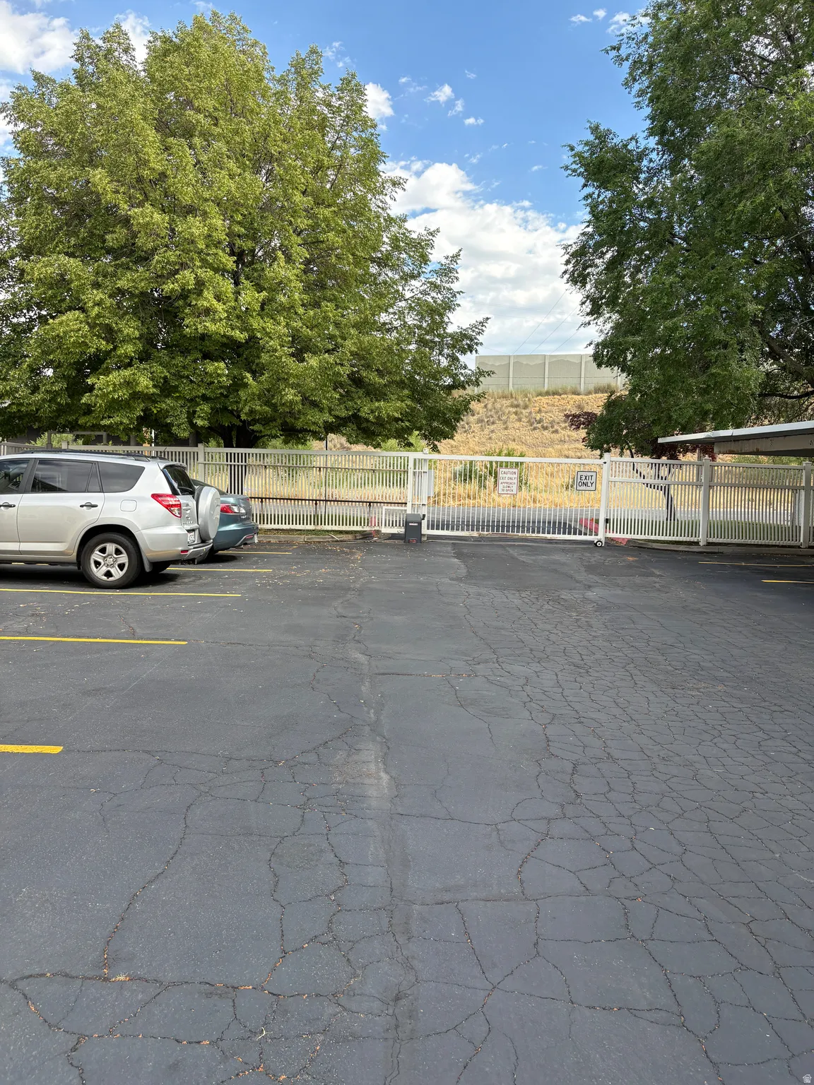 Paved parking area with yellow striped parking spaces, featuring a white metal gate and fencing