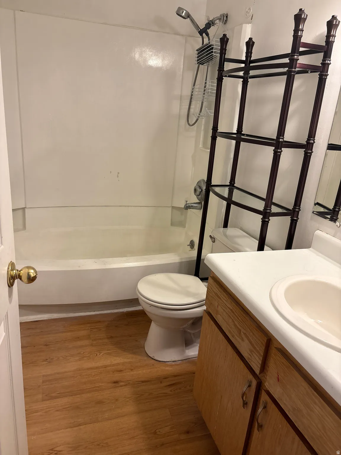 Bathroom featuring a white bathtub with an integrated shower, wood-finish flooring, and a vanity with a white countertop and integrated sink