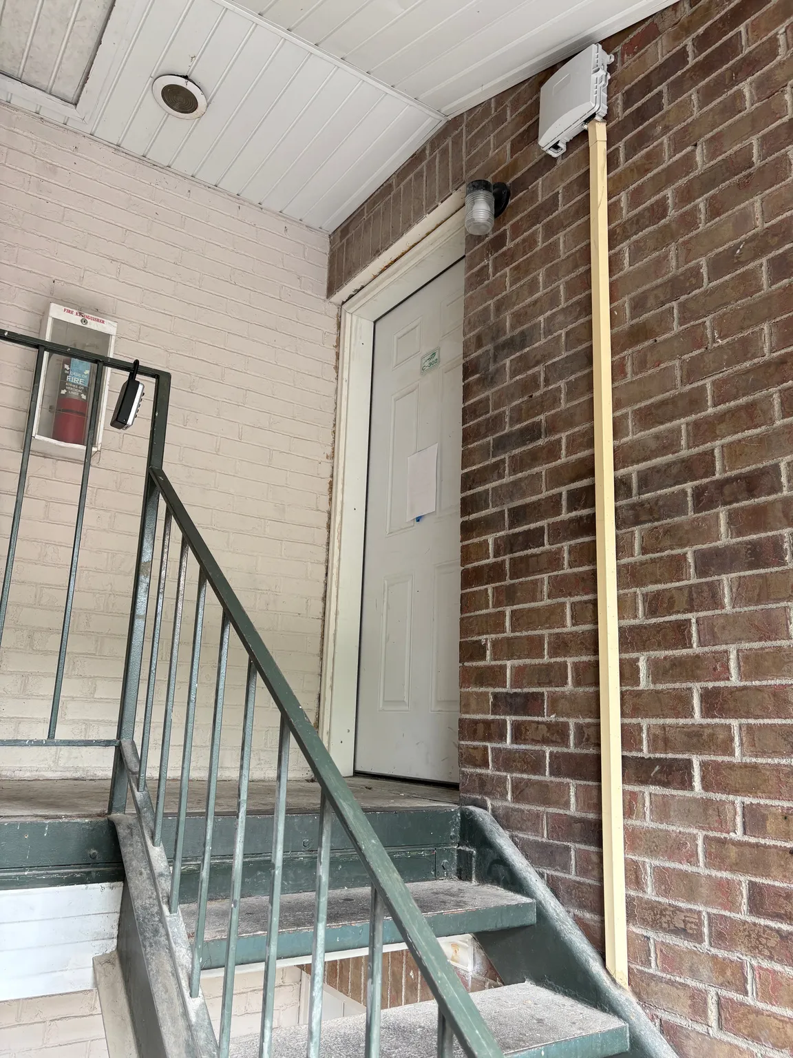 Entryway featuring a white door, brick exterior walls, and a metal railing
