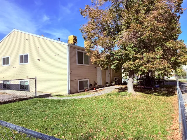 Two-story exterior with light-colored siding, multiple windows, and a mature tree providing shade