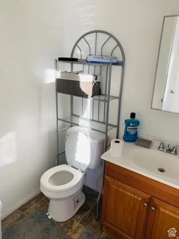 Bathroom featuring a white toilet, wood-finish vanity with a white countertop and integrated sink, and patterned flooring