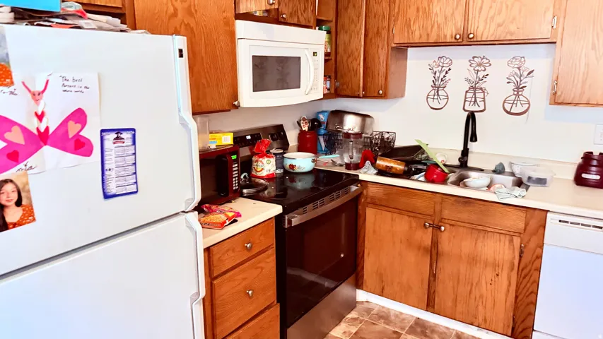 Kitchen featuring wood cabinetry, white appliances, and a black cooktop