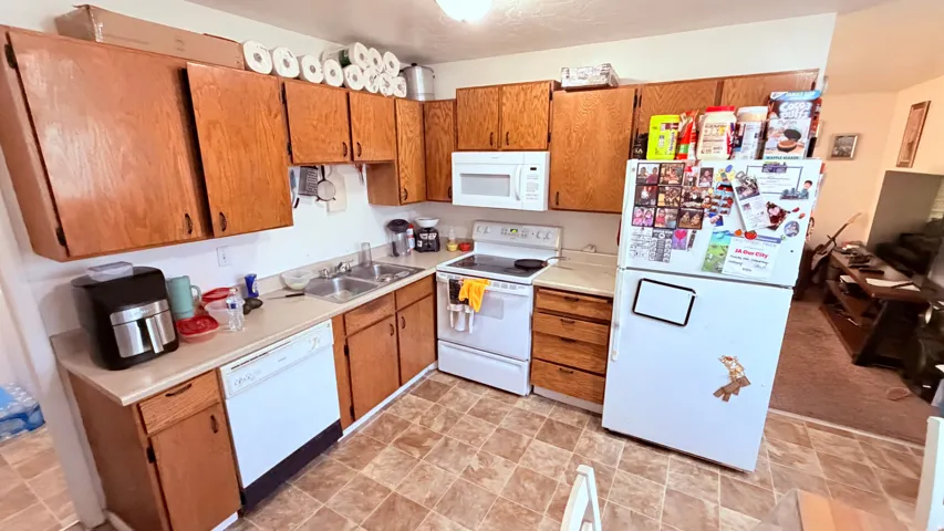 Kitchen featuring wood-finish cabinetry, light-toned countertops, a white dishwasher, a double basin sink, and a white oven/range with an overhead microwave
