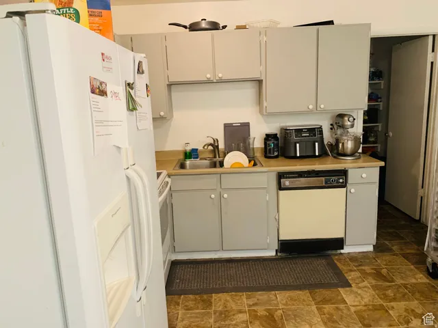 Kitchen featuring light gray cabinetry with white knob hardware, a stainless steel sink, beige countertops, and a built-in dishwasher