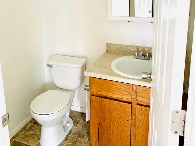 Bathroom featuring a white toilet, wood-finish vanity with a laminate countertop, and a white porcelain sink with a chrome faucet