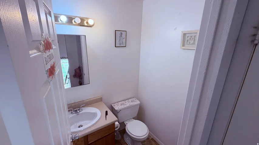 Bathroom featuring a single vanity with a white basin and a laminate countertop, a standard toilet, and a polished chrome light fixture with three bulbs