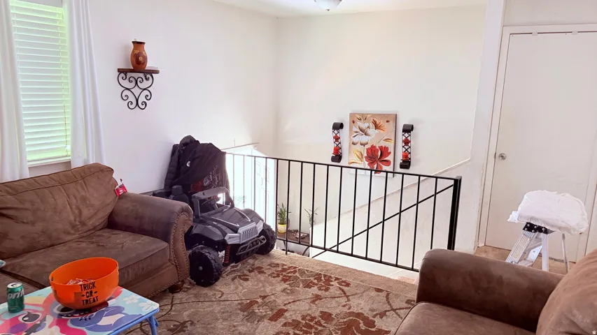 Interior open concept space featuring light-colored walls and a stairwell with a black metal railing