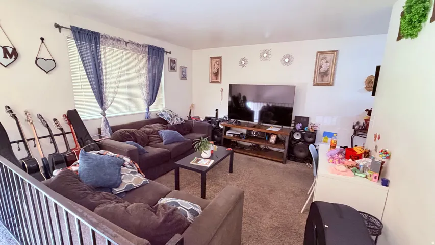 Living area with wall-to-wall carpeting and a large window featuring horizontal blinds