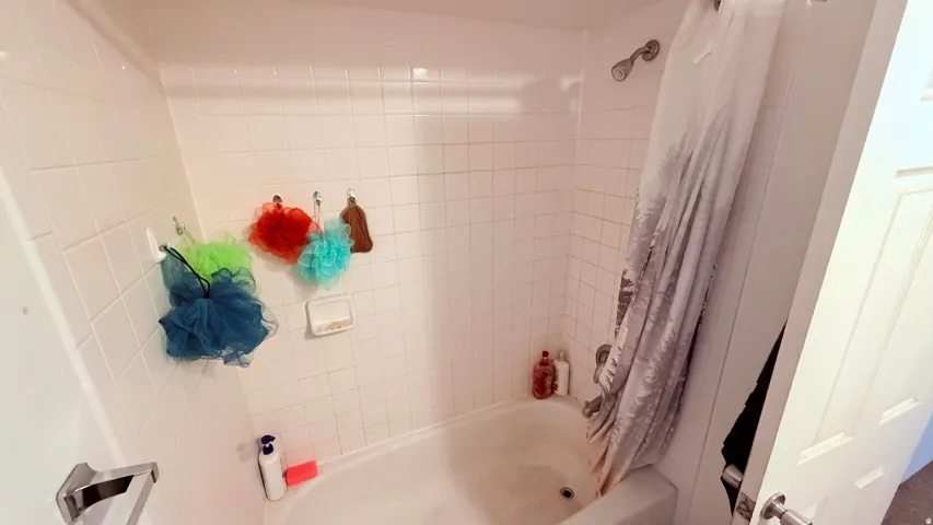 White tile surround with a built-in tub, chrome shower head, and matching chrome fixtures