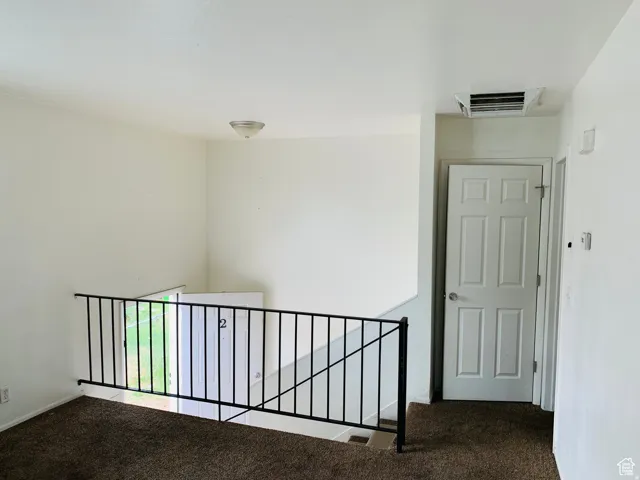 Upper-level landing featuring neutral-toned walls, brown carpeting, a white paneled door, a ceiling-mounted light fixture, and a black metal railing