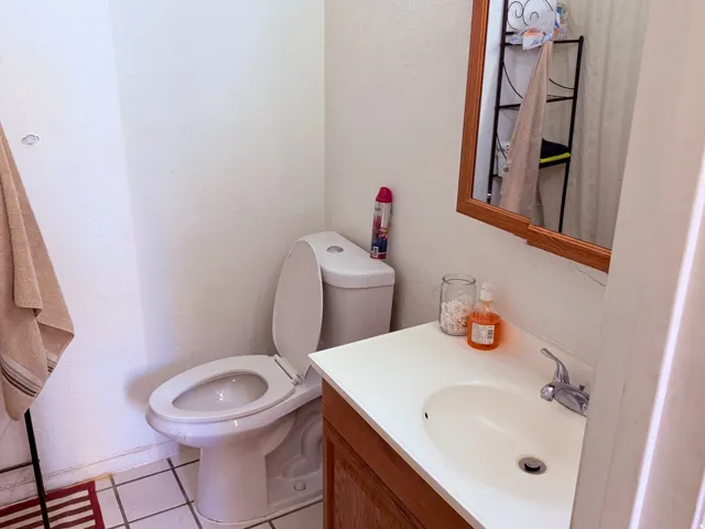 Bathroom featuring a white toilet, wood-finish vanity with a white countertop and integrated sink, chrome faucet, and a wood-framed mirror