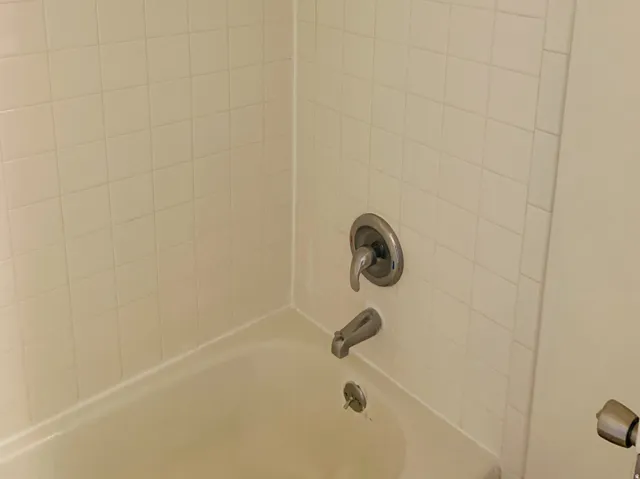 White tiled shower surround with a built-in bathtub and chrome fixtures