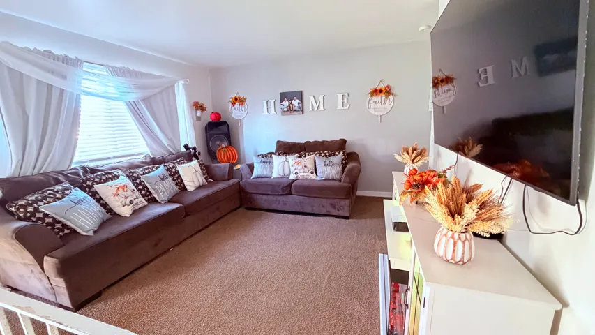Living area featuring neutral wall paint, carpeted flooring, and a large window with blinds