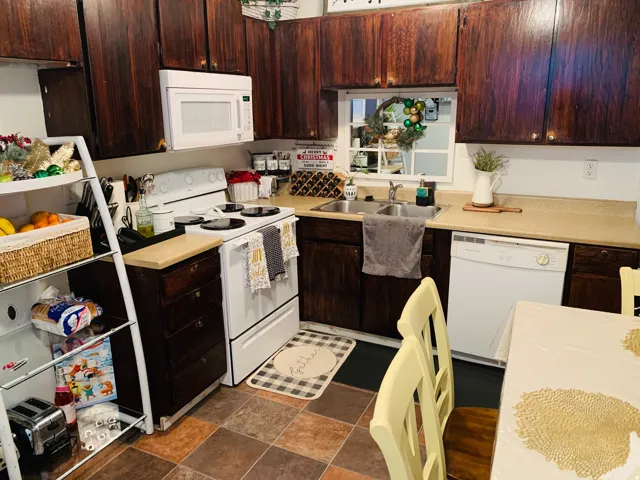 Kitchen featuring dark wood-finish cabinetry, white appliances, and a double basin sink