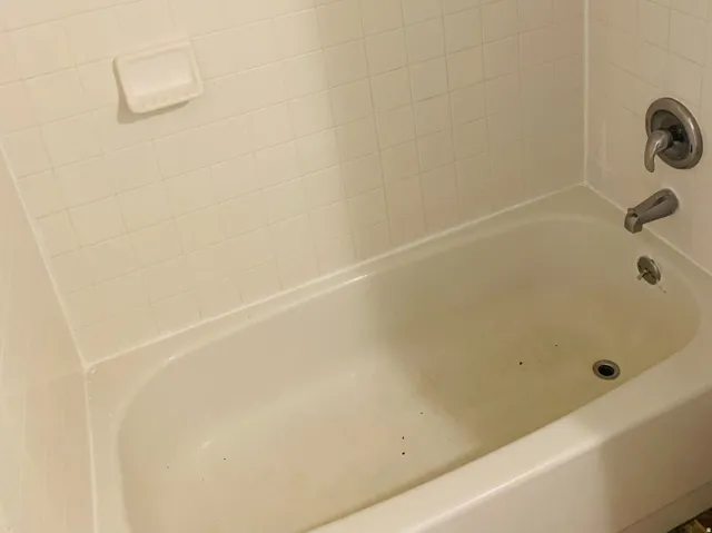 White tile bathtub surround featuring a built-in soap dish and chrome fixtures