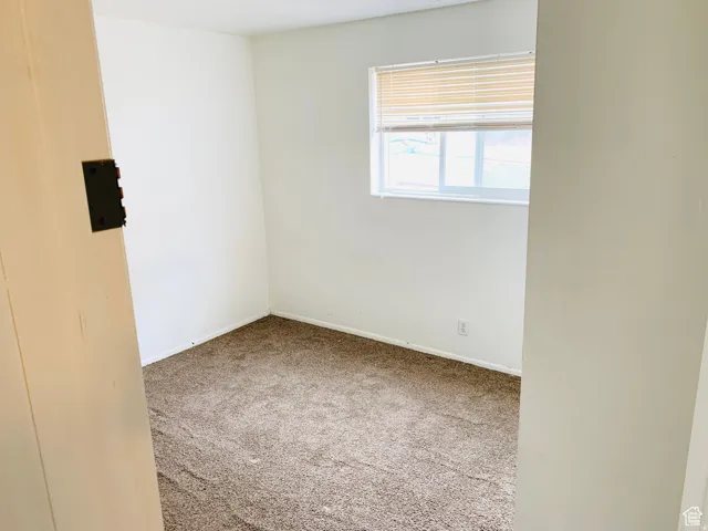 Carpeted room with white walls, baseboards, and a single window featuring horizontal blinds