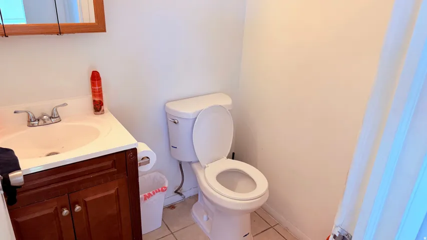 Bathroom featuring a wood-finish vanity with a white countertop and integrated sink, a two-piece toilet, and tile flooring