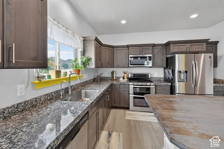 Kitchen featuring ample dark wood cabinetry, stainless steel appliances, granite countertops, and a wood-finish flooring