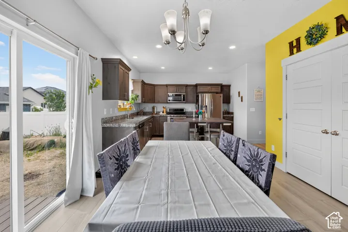 Open-concept kitchen and dining area featuring light wood-finish flooring, a contemporary chandelier, recessed lighting, and sliding glass door access to the exterior